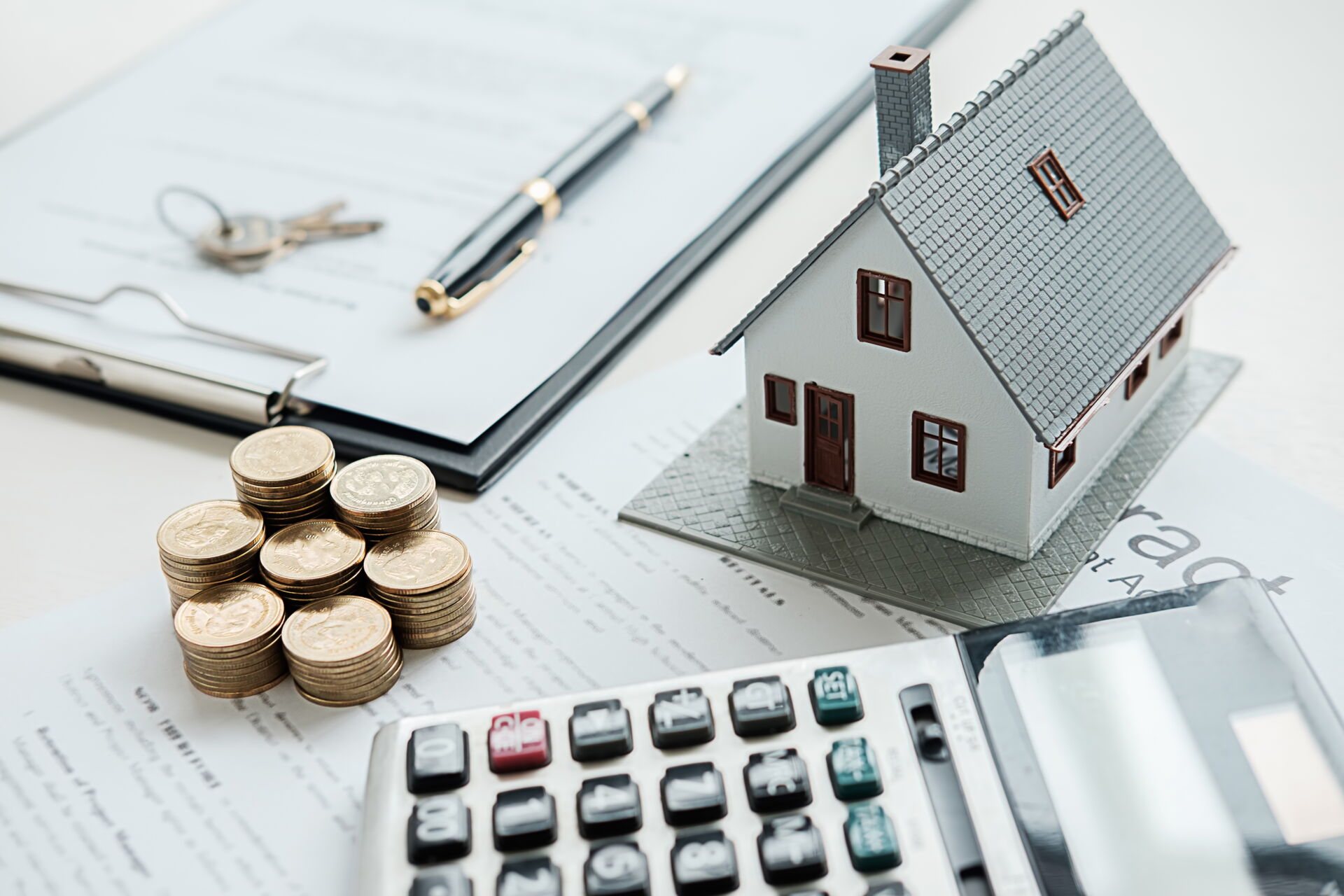 Hausmodell, Geldstapel, Taschenrechner, Schlüssel und Vertrag. Symbol für Immobilienkauf mit SCHULER INVESTMENTS. Finanzierung und Beratung.
